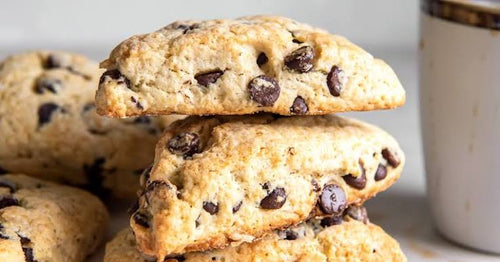 A stack of Gluten Free golden-brown chocolate chip scones with dark chocolate chips, shown with a white mug partially visible on the right.